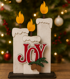Decorative sign with 'JOY' and candles against a Christmas tree background