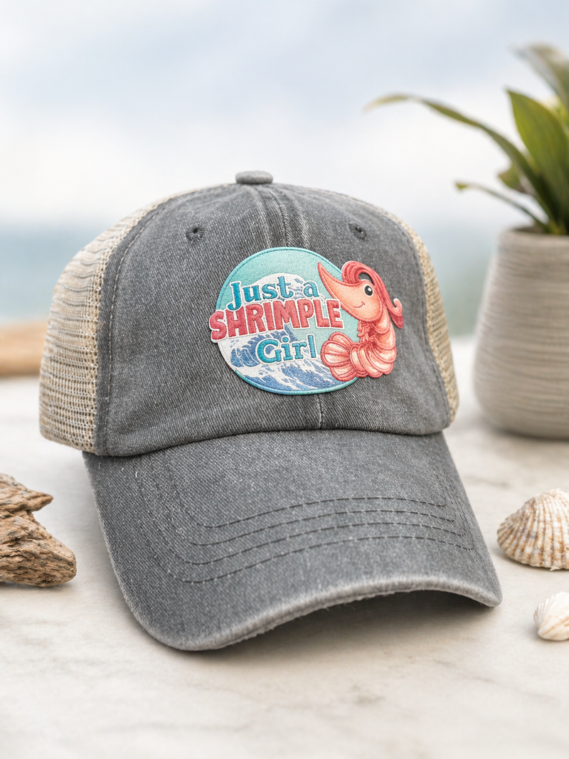 Gray cap with 'Just a Shrimple Girl' graphic on a beach setting