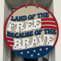Decorative sign with 'Land of the Free Because of the Brave' text on a beige background.