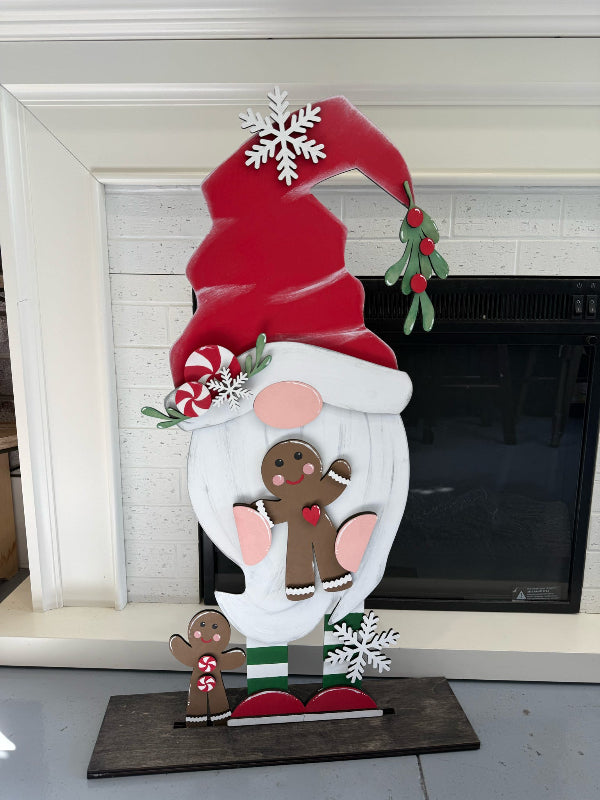 Decorative Christmas gnome with a red hat and gingerbread men in front of a fireplace.