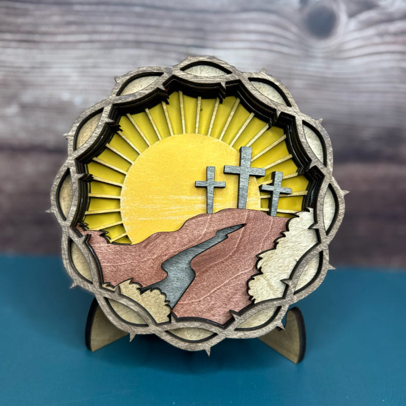 A layered wooden crown of thorns with crosses, placed on a stand, against a backdrop of a wooden plank.