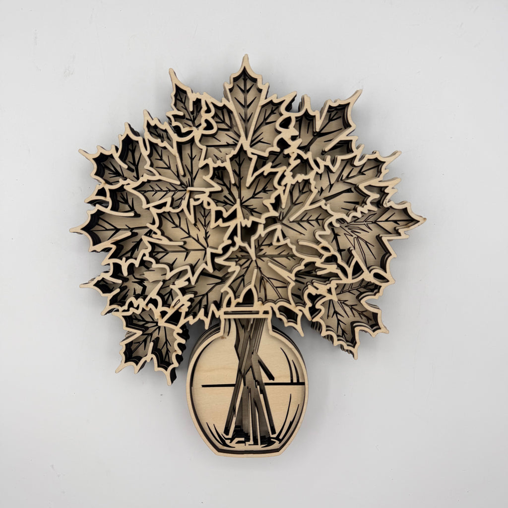 Laser-cut wooden wall art featuring layered maple leaves in a vase, shown against a plain light gray background.