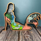 A decorative layered mermaid sign with a unique design, featuring a silhouette of a mermaid in multicolor layers, mounted on a wooden surface.