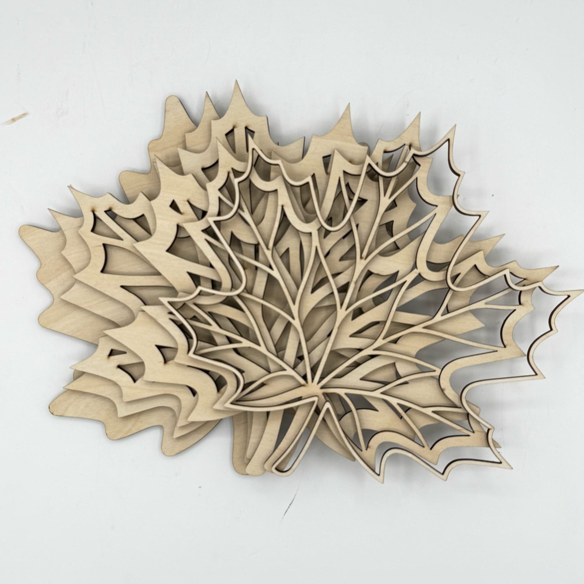 A 3D layered wooden wall art piece shaped like a maple leaf, made from laser-cut natural wood, displayed on a plain white background.