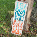 Wooden sign with 'Let our lives be full of thanks' text on grass