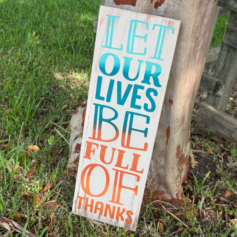 Wooden sign with 'Let our lives be full of thanks' text on grass