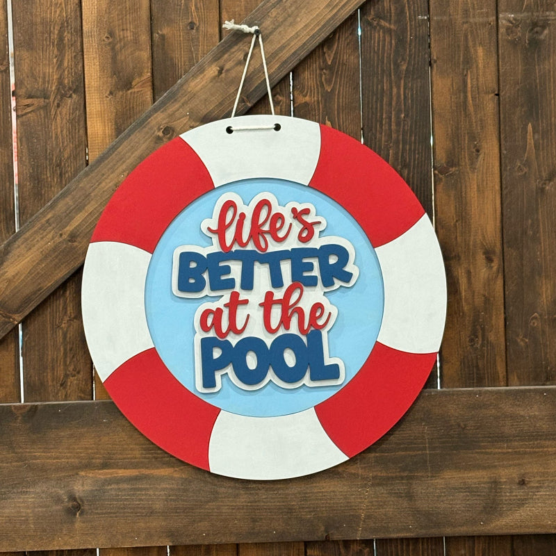Decorative sign with 'Life's Better at the Pool' text on a wooden fence background