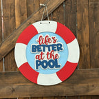 Decorative sign with 'Life's Better at the Pool' text on a wooden fence background