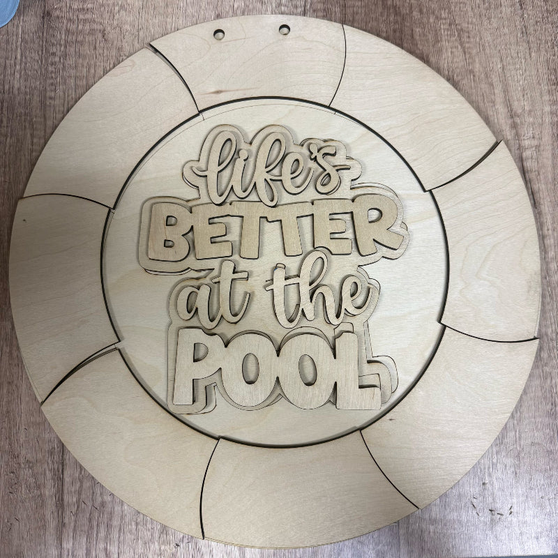 Wooden circular sign with 'Life's Better at the Pool' text on a wooden surface