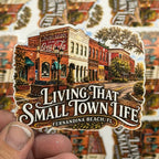 Sticker of a small town scene with 'Living That Small Town Life' text, held over a sheet of similar stickers.
