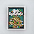 A square framed wall art piece featuring a stylized pineapple with the words “Mele Kalikok’a” in white script across the top, set against a teal background with multicolored string lights and a white frame.