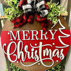 A round door hanger with a Christmas tree design and the text 'Merry Christmas' written in a playful font, decorated with a red and black plaid ribbon on top.