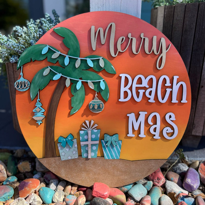 Decorative sign with 'Merry Beach Mas' text, palm tree, and presents on a colorful stone background.