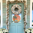 Decorative wreath with shells and garland on a teal door with a 'Merry Beach Mas' sign.