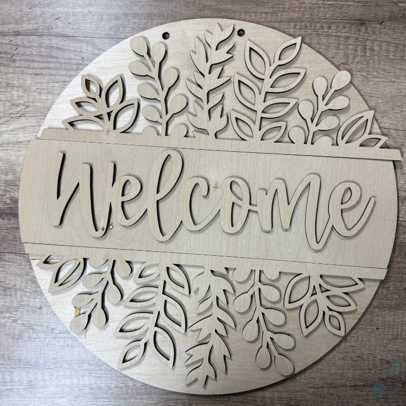 Decorative wooden sign with 'Welcome' text and leaf patterns on a wooden surface