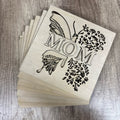 Stack of wooden cutouts with 'MOM' and floral designs on a wooden surface