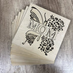 Stack of wooden cutouts with 'MOM' and floral designs on a wooden surface