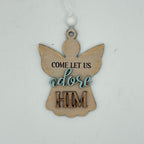 A wooden angel-shaped Christmas ornament with the words 'COME LET US adore HIM' printed on it, hanging against a plain light gray background.