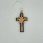 A wooden Christmas ornament shaped like a cross with a laser-cut star in the center, hanging from a white cord with a white bead against a light gray background.