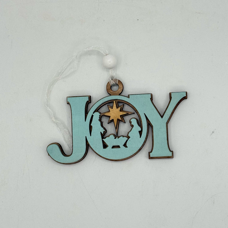 A light blue wooden Christmas ornament spelling out 'JOY' with a Nativity scene cutout in the center, hanging from a white string with a white bead, on a light gray background.