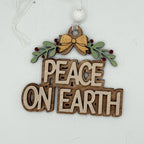A wooden hanging ornament with the words “PEACE ON EARTH” in raised natural wood letters, decorated with green holly leaves, small red berries, and a gold bow at the top, suspended by a white ribbon and white bead.