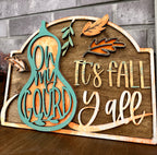 A wooden laser sign with cut-out words and autumn leaf designs, featuring the text 'Oh My Gourd It's Fall Y'all'.