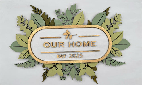 Decorative sign with 'Our Home Est. 2025' text surrounded by green leaves on a white background