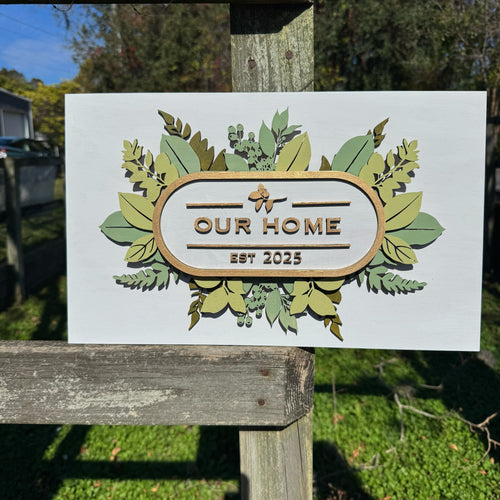 Decorative sign with 'Our Home Est 2025' on a wooden post outdoors.