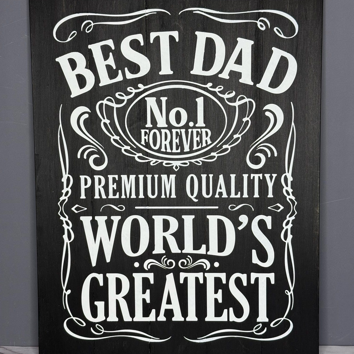 Decorative sign with text 'Best Dad No.1 Forever Premium Quality World's Greatest' on a dark background