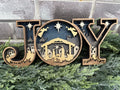 A 3D Christmas sign with the word 'JOY' where each letter represents a scene from the nativity story, set against a night background with stars.
