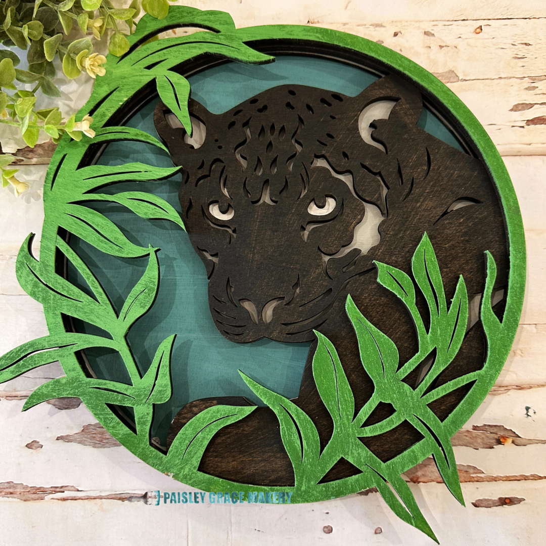 A decorative wooden sign featuring a cut-out design of a tiger with leaves around it, predominantly in shades of brown and green.