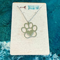 Necklace with paw print and heart pendant on a branded card against a blue textured background