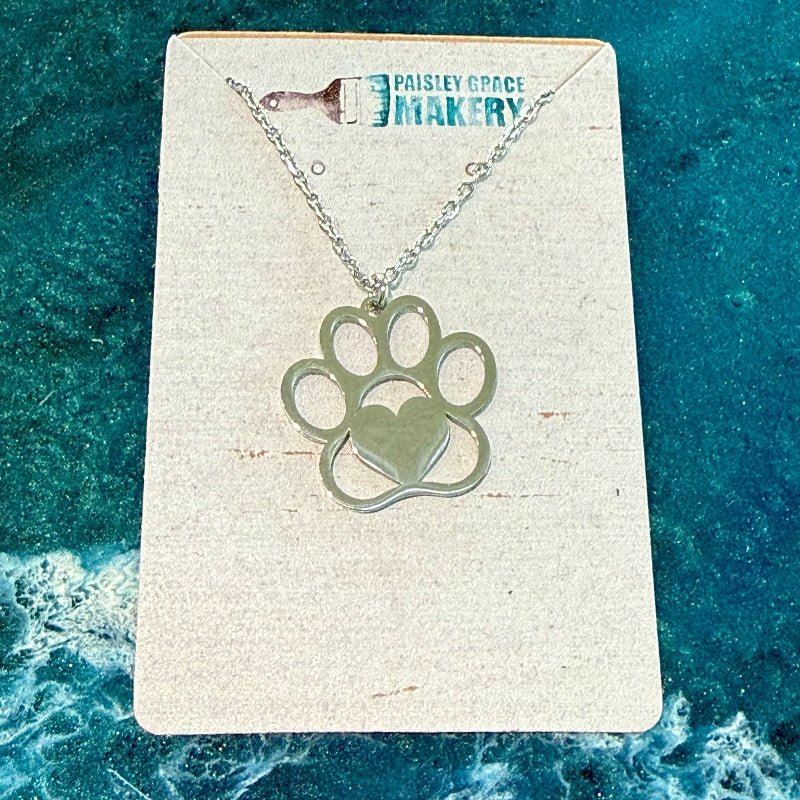 Necklace with paw print and heart pendant on a branded card against a blue textured background