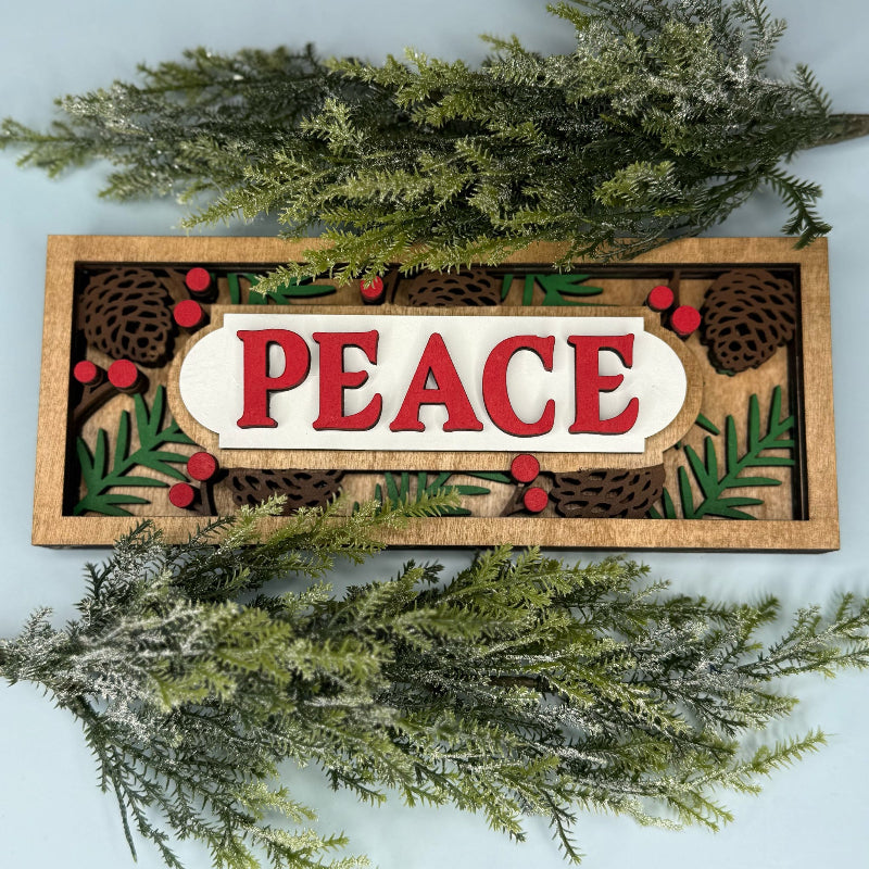 Decorative sign with 'PEACE' surrounded by greenery on a light blue background