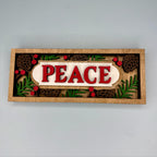 Decorative sign with 'PEACE' text surrounded by Christmas-themed elements on a plain background