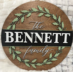 Round wooden sign with 'The Bennett Family' text and green leaf design on a white textured background
