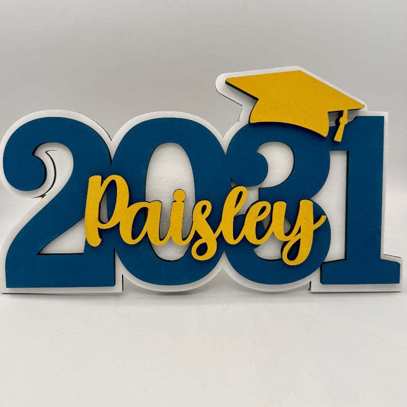 Decorative sign with '2021 Paisley' text and a yellow graduation cap on a white background