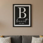 Framed print with a large white letter 'B' and the name 'bennett' with 'EST 2008' below, against a light blue wooden background.