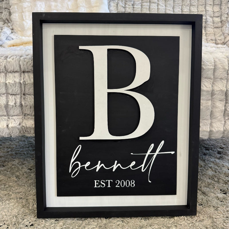 Framed artwork with a large white letter 'B' and the name 'bennett' below on a black background.