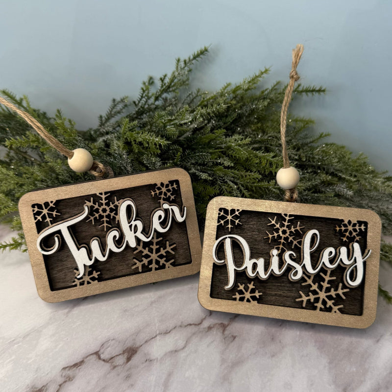 Two wooden name tags with 'Tucker' and 'Paisley' on a marble surface with greenery in the background.