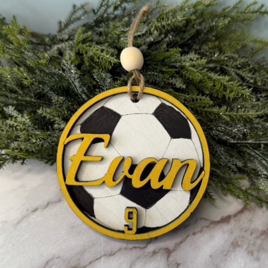 Soccer ball design ornament with 'Evan' and number '9' on a marble surface with greenery in the background