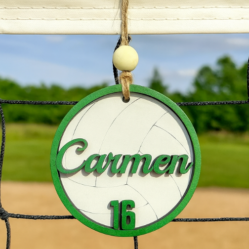 Decorative volleyball net charm with 'Carmen' and number '16' on a volleyball net against a blurred outdoor background.