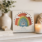 Decorative plaque with rainbow and paw print design on a shelf with candles and plants.