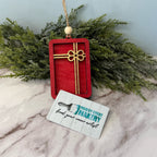 Red decorative tag with gold cross and 'Paisley Grace Makery' card on marble surface with greenery