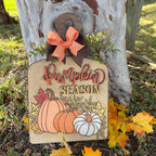 Decorative sign with 'Pumpkin Season' text and pumpkins, tied with a bow, against a rustic background.