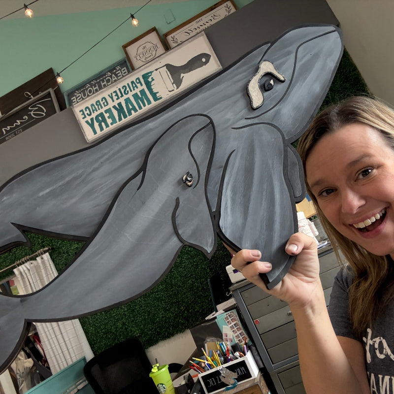 Woman holding a large cardboard cutout of a whale in an indoor setting with decorative elements.