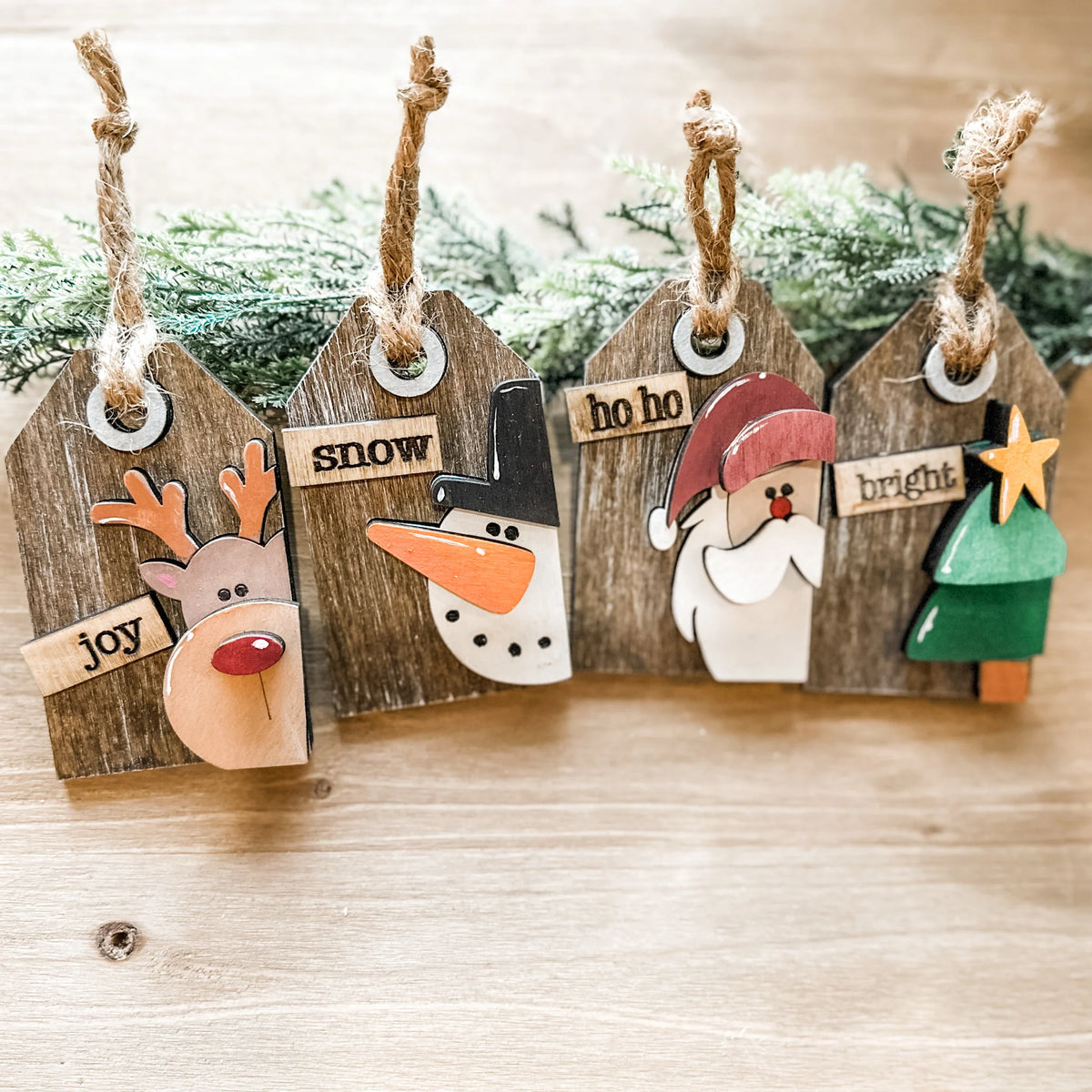 Four rustic wood ornament tags with reindeer, snowman, Santa and Christmas tree designs and twine hangers