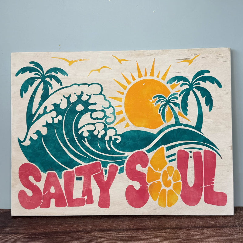 Decorative sign with 'Salty Soul' text, wave, sun, and palm trees on a wooden surface.