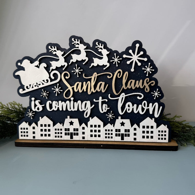 Decorative sign with 'Santa Claus is coming to town' text and Christmas elements on a white background.