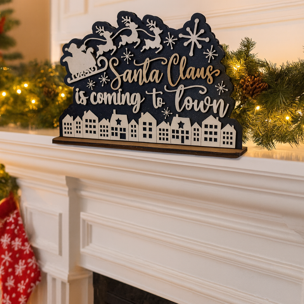 Decorative sign with 'Santa Claus is coming to town' on a fireplace mantel with Christmas decorations.